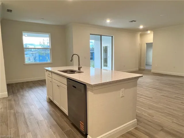 Kitchen featuring white cabinetry, light wood-type flooring, dishwasher, light stone counters, and crown molding