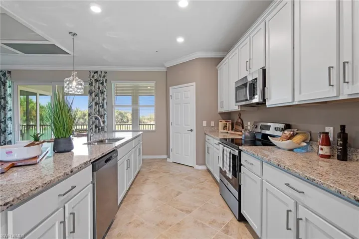 Kitchen with a sink, ornamental molding, white cabinetry, light stone countertops, and stainless steel appliances