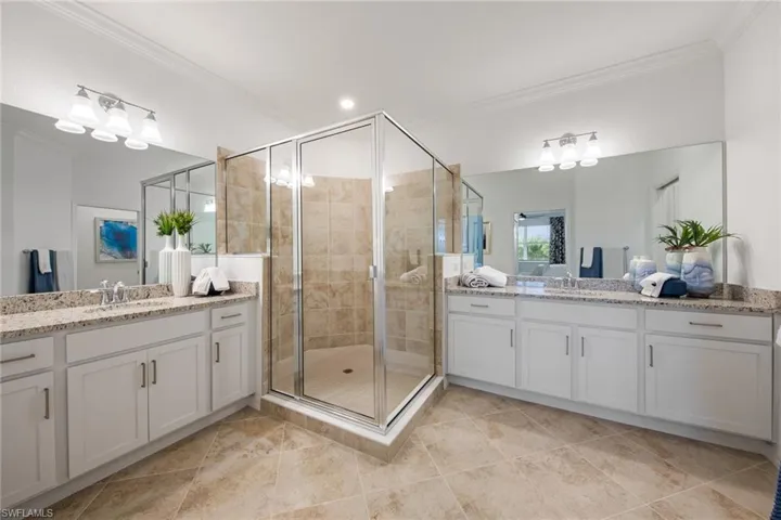 Full bathroom featuring a sink, ornamental molding, two vanities, and a shower stall