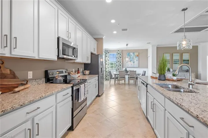 Kitchen with hanging light fixtures, a sink, white cabinets, and stainless steel appliances