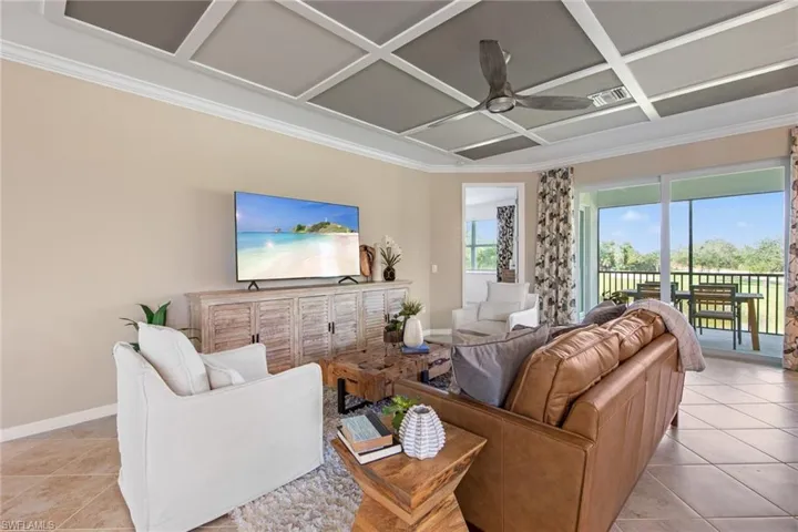 Living room with light tile patterned floors, baseboards, ornamental molding, a ceiling fan, and coffered ceiling