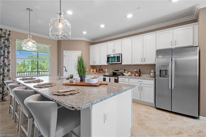 Kitchen featuring white cabinetry, crown molding, light stone countertops, a kitchen island with sink, and stainless steel appliances