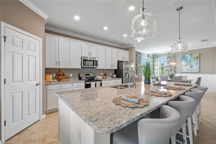 Kitchen featuring white cabinets, a sink, appliances with stainless steel finishes, crown molding, and a spacious island