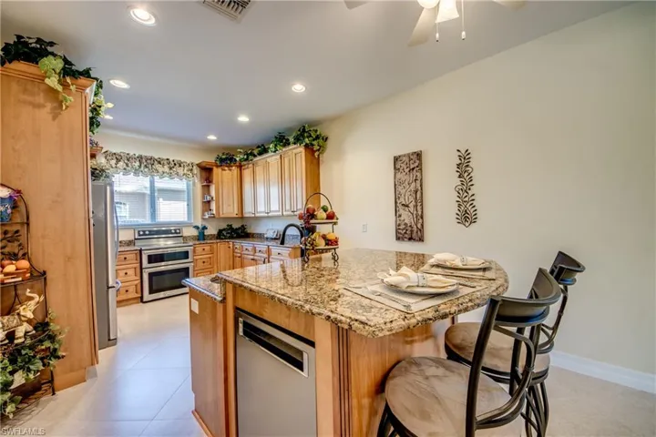 Kitchen featuring stainless steel appliances, a peninsula, a breakfast bar, light stone counters, and open shelves