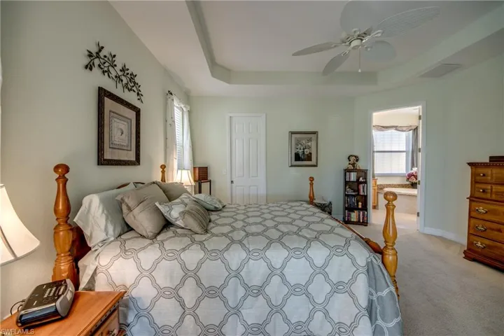 Bedroom with light carpet, a raised ceiling, ceiling fan, and ensuite bath