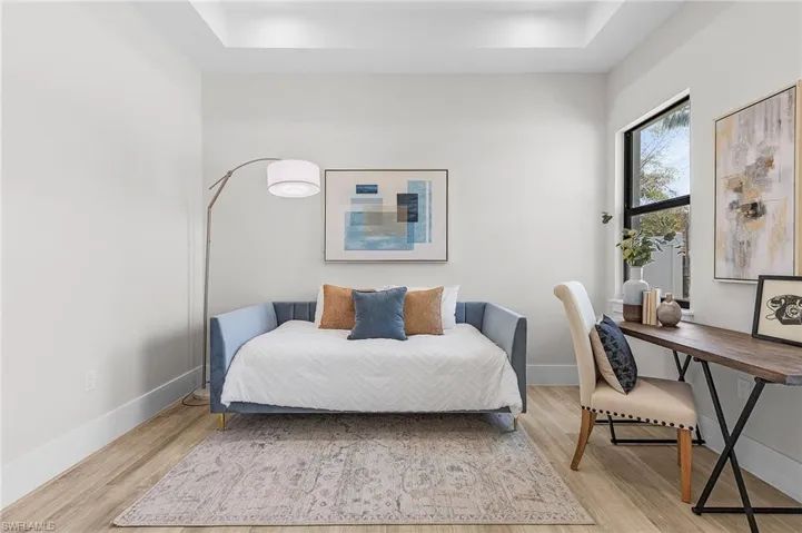 Bedroom with light wood-style flooring, a tray ceiling, and baseboards