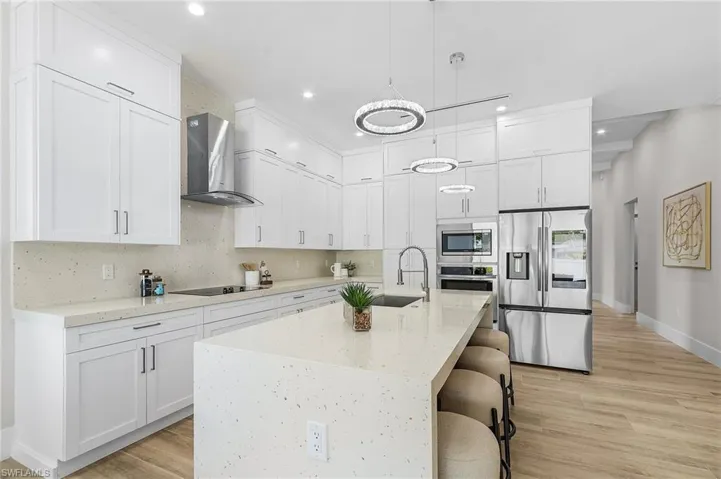 Kitchen with stainless steel appliances, wall chimney range hood, recessed lighting, a sink, and white cabinets