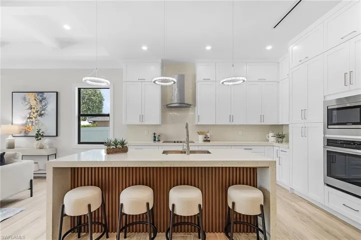 Kitchen featuring appliances with stainless steel finishes, wall chimney exhaust hood, light wood-style floors, recessed lighting, and a kitchen bar