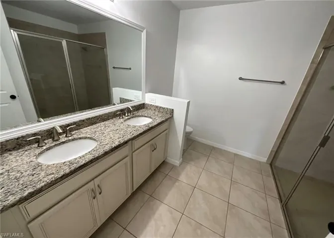 Bathroom featuring a double vanity with stone countertops, a large framed mirror, tiled flooring, and a glass-enclosed shower