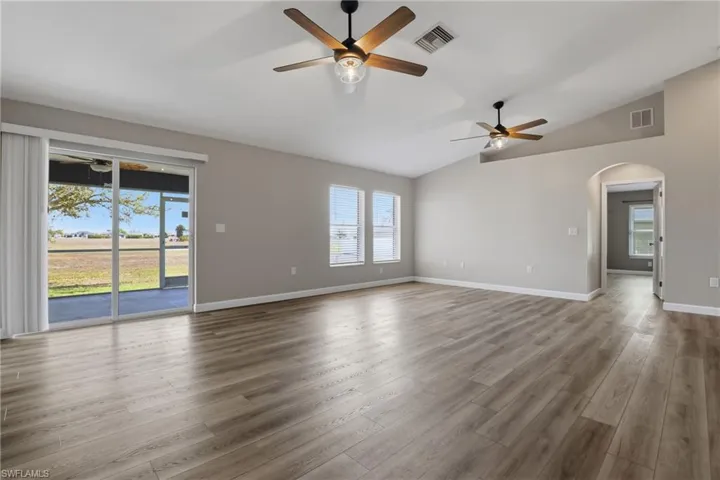 Unfurnished room featuring a ceiling fan, arched walkways, vaulted ceiling, and dark wood-type flooring