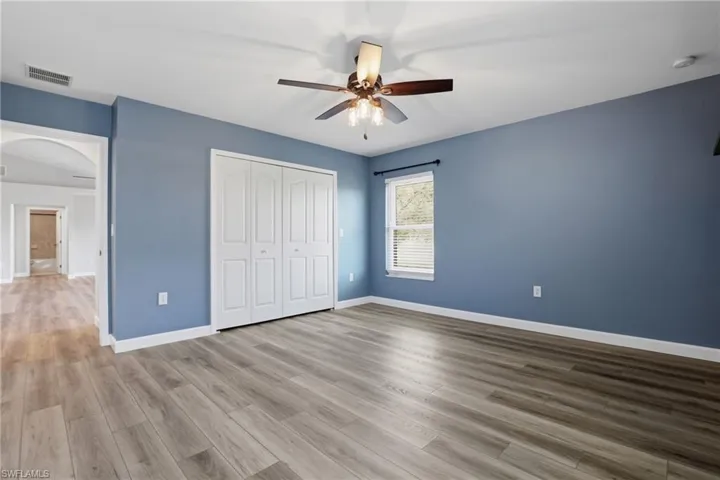 Unfurnished bedroom with arched walkways, a closet, ceiling fan, and light wood-style flooring