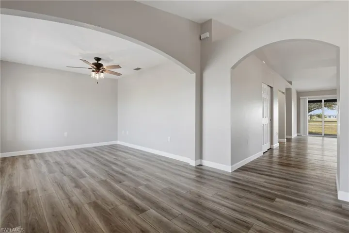 Unfurnished room featuring arched walkways, ceiling fan, and dark wood finished floors