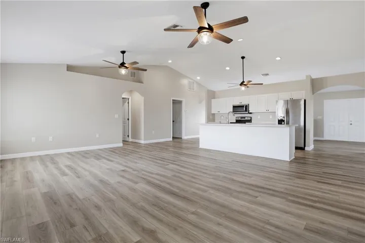 Unfurnished living room featuring arched walkways, light wood-type flooring, a high ceiling, recessed lighting, and ceiling fan
