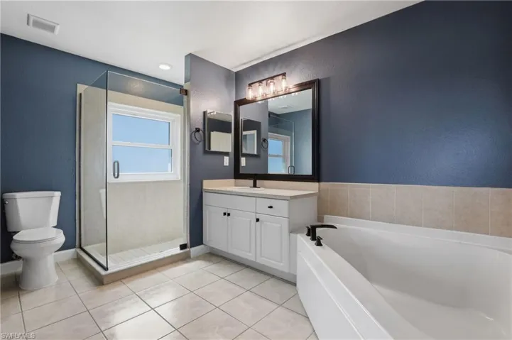 Full bath with a textured wall, a garden tub, vanity, a stall shower, and light tile patterned flooring
