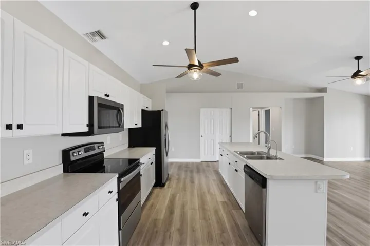 Kitchen with stainless steel appliances, a ceiling fan, white cabinetry, light countertops, and light wood-style flooring
