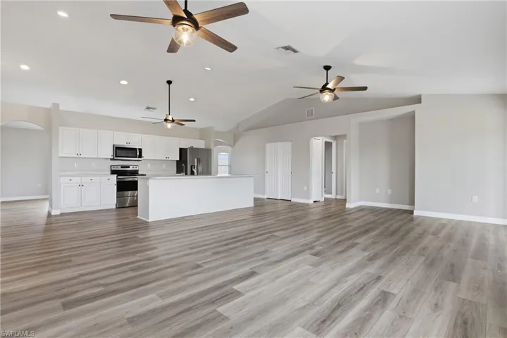 Unfurnished living room featuring arched walkways, light wood-style floors, and lofted ceiling