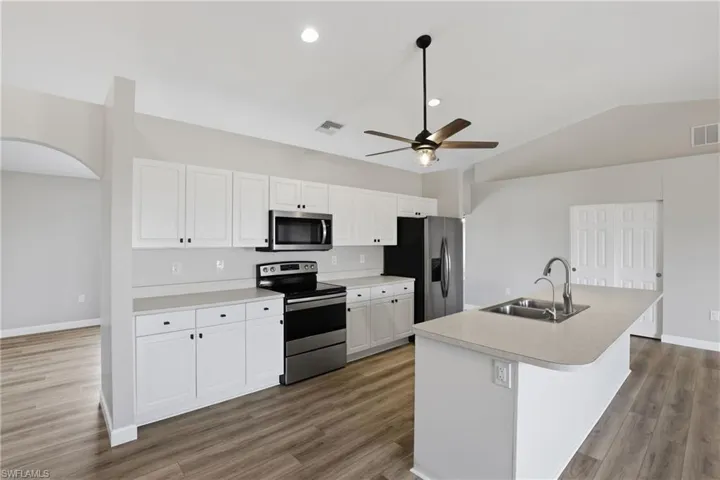 Kitchen with stainless steel appliances, a center island with sink, white cabinetry, arched walkways, and light countertops