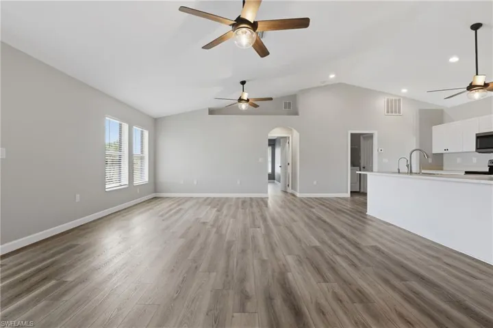 Unfurnished living room with a ceiling fan, arched walkways, light wood-style flooring, a high ceiling, and recessed lighting