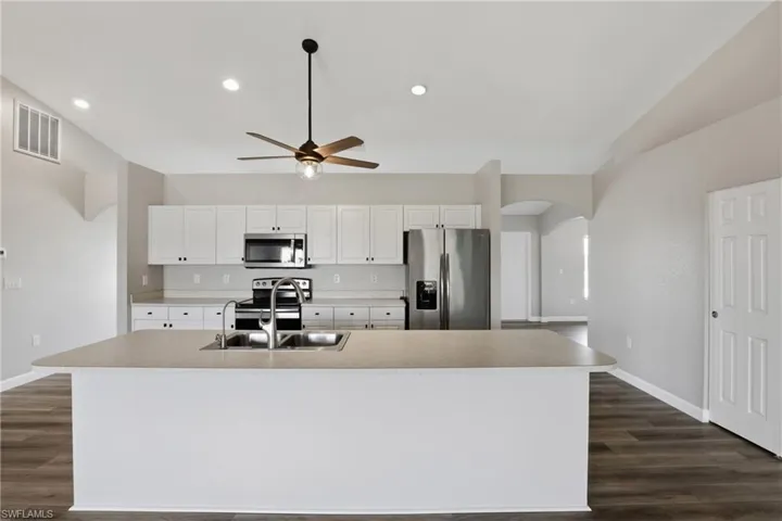 Kitchen featuring arched walkways, white cabinets, stainless steel appliances, light countertops, and an island with sink
