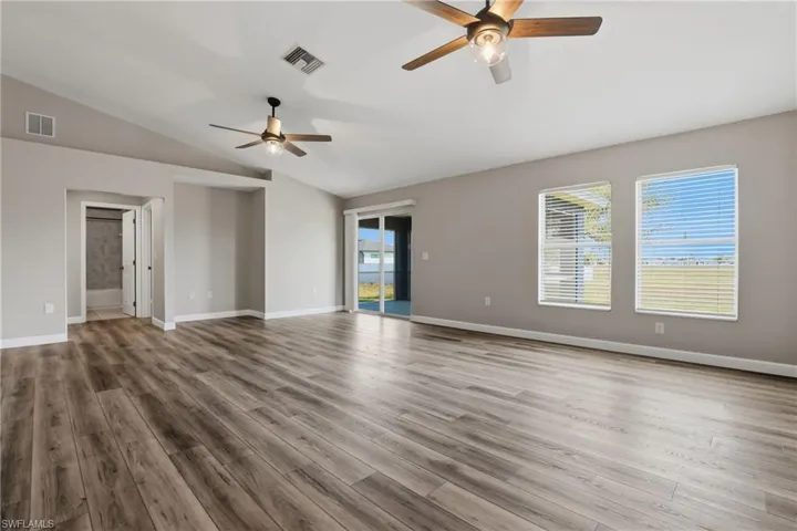 Empty room with ceiling fan, lofted ceiling, and dark wood-style flooring