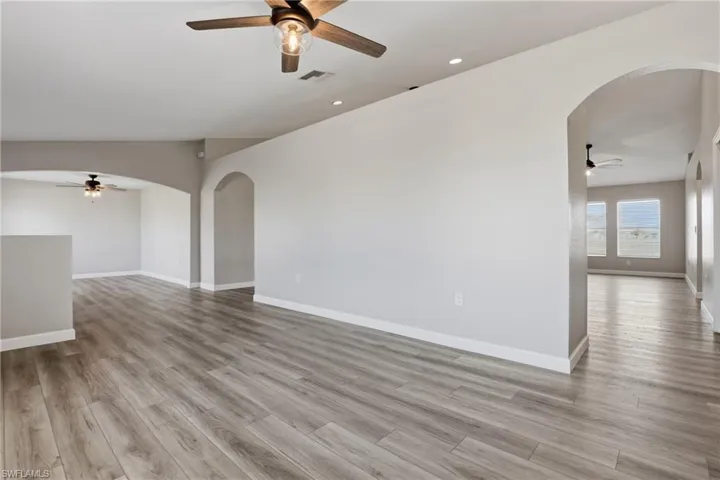 Spare room featuring ceiling fan, arched walkways, light wood-style floors, lofted ceiling, and recessed lighting