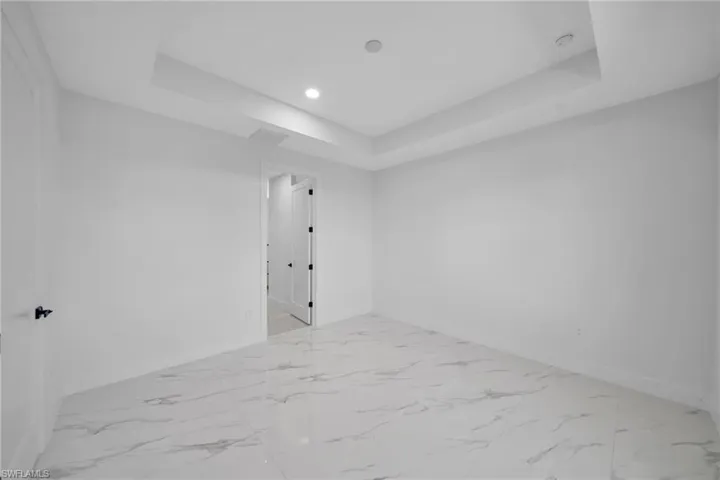 Empty room with a tray ceiling, recessed lighting, and light marble finish floors