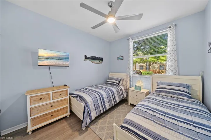 Bedroom featuring light blue walls, two beds with striped bedding, a window with blinds, and a ceiling fan