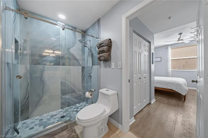 The bathroom features a spacious glass-enclosed shower with blue-toned tile work and a white toilet