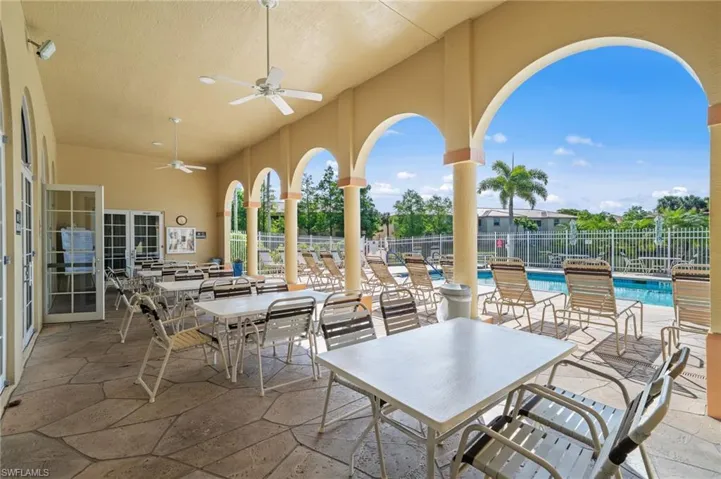 Covered patio area with a flagstone floor, featuring ceiling fans and seating, overlooking a swimming pool