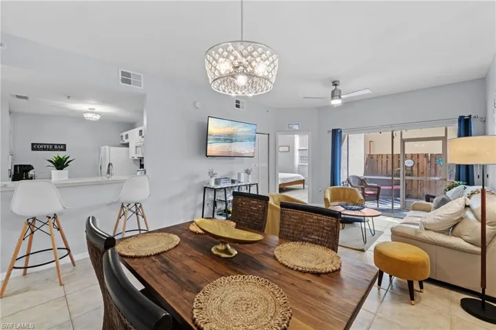 This bright open-concept living space features light-colored walls, tile flooring, and a sliding glass door leading to an outdoor patio area