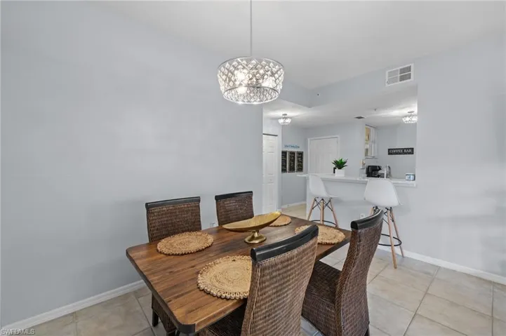 Dining area featuring a modern chandelier, light-colored walls, tiled flooring, and a view of the breakfast bar