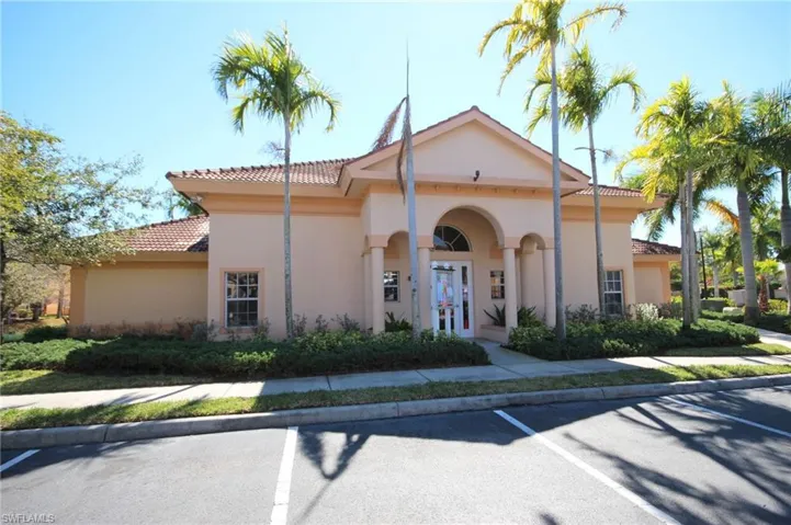 This property features a stucco exterior with a tiled roof, an arched entry, and prominent palm trees