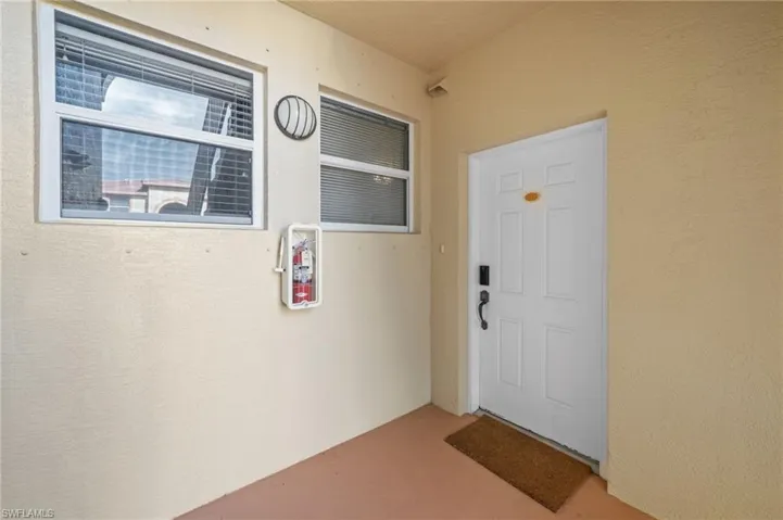 This property features a white panel door with dark hardware, a security camera, and two windows with blinds
