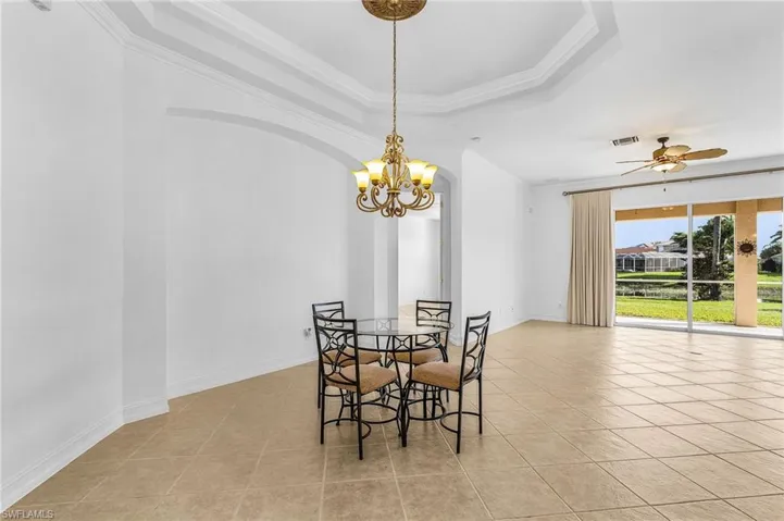 Dining space with a chandelier, light tile patterned flooring, crown molding, a ceiling fan, and a raised ceiling