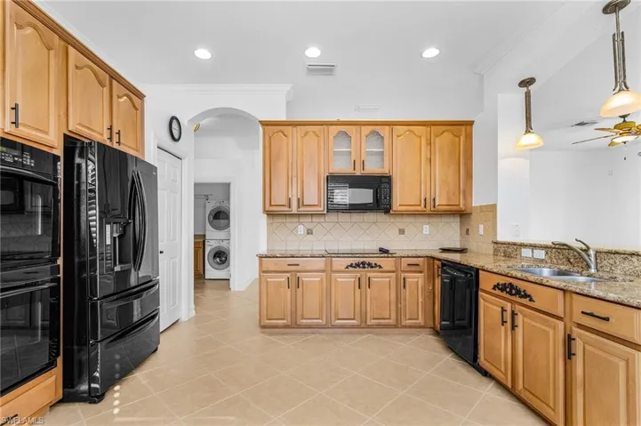 Kitchen featuring black appliances, stacked washer / dryer, light stone countertops, crown molding, and arched walkways
