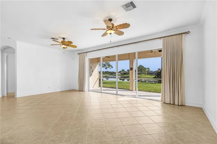 Unfurnished room featuring crown molding, a ceiling fan, a water view, arched walkways, and light tile patterned flooring