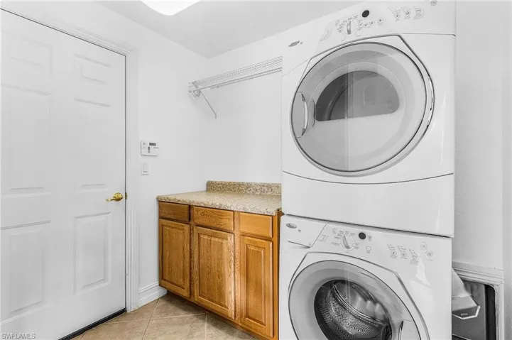 Washroom featuring stacked washer and clothes dryer, cabinet space, and light tile patterned floors