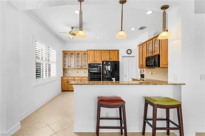 Kitchen with black appliances, ornamental molding, glass insert cabinets, a peninsula, and brown cabinetry