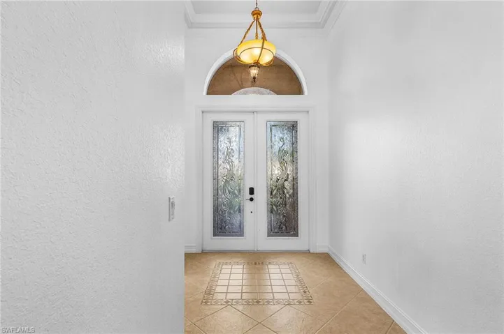 Foyer with french doors, light tile patterned floors, a textured wall, and ornamental molding