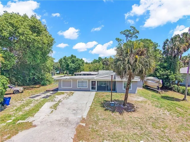 The property features a grey exterior with a screened porch, a paved driveway, and mature trees