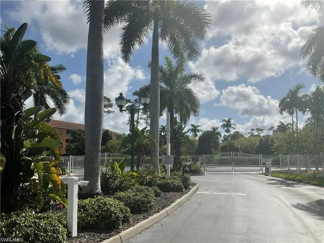 View of asphalt road featuring a gate, curbs, a gated entry, and street lighting