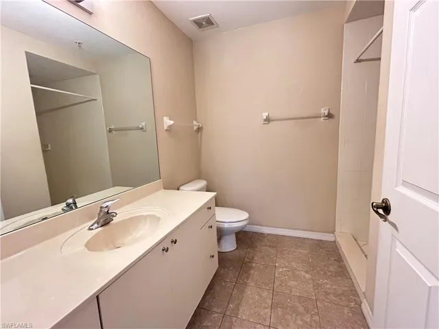 Full bathroom with a tile shower, vanity, and dark tile patterned flooring