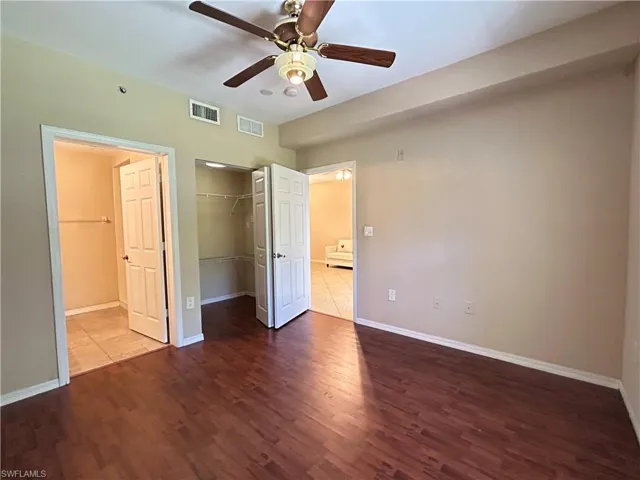 Unfurnished bedroom with dark wood-style floors, a spacious closet, and a ceiling fan