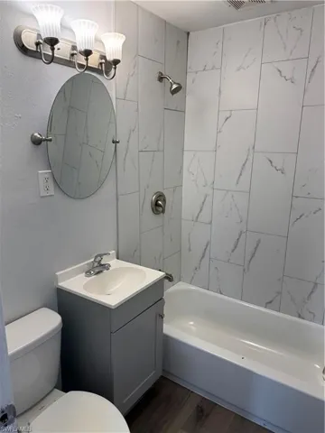 Guest Bathroom with vanity, dark wood finished LVP floors, and washtub / shower combination