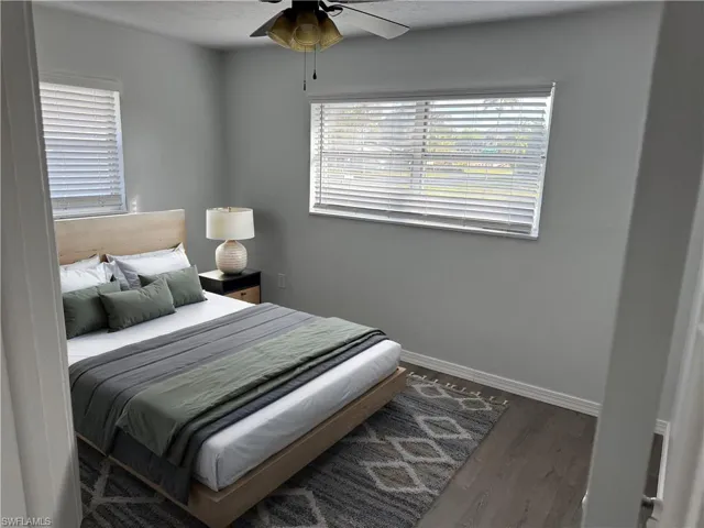 Virtually Staged - Front Guest Bedroom featuring ceiling fan, dark wood-style LVP floors, and multiple windows