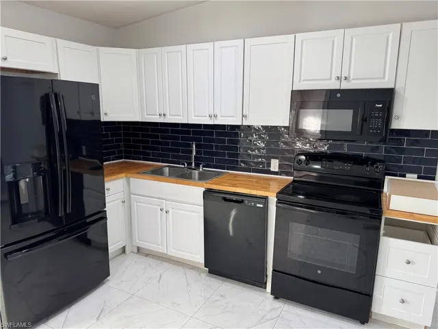 Kitchen featuring black appliances, white cabinetry, light marble finish tile flooring, butcher block countertops and tile backsplash