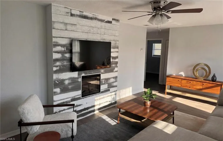 Virtually Staged - Living area with wood-style LVP floors, a glass covered fireplace, and ceiling fan