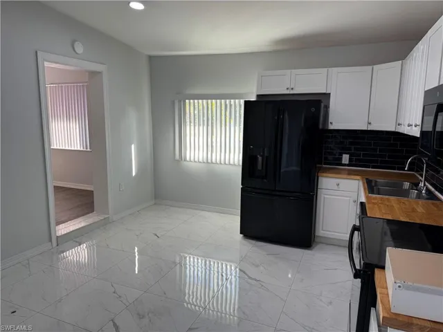 Kitchen featuring black appliances, white cabinetry, light marble finish tile flooring, butcher block countertops and tile backsplash. View towards Living Room entry.