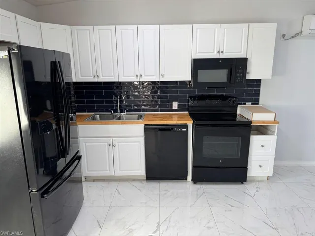 Kitchen featuring black appliances, white cabinetry, light marble finish tile flooring, butcher block countertops and tile backsplash