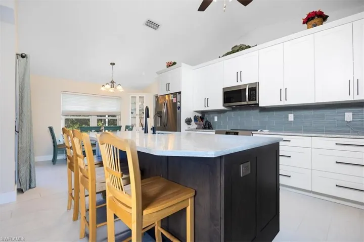 Kitchen featuring an island with sink, vaulted ceiling, two tone cabinets, a kitchen breakfast bar, and stainless steel appliances